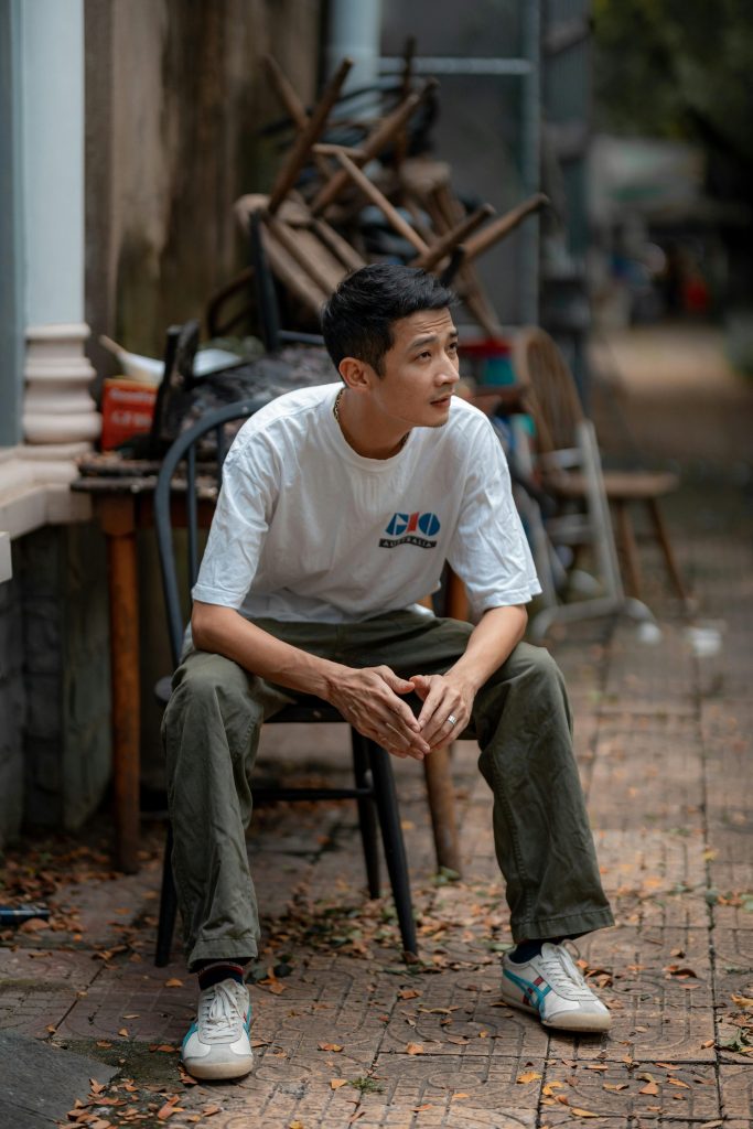 Young man in casual attire sitting outdoors, surrounded by chairs in Bien Hoa, Vietnam.